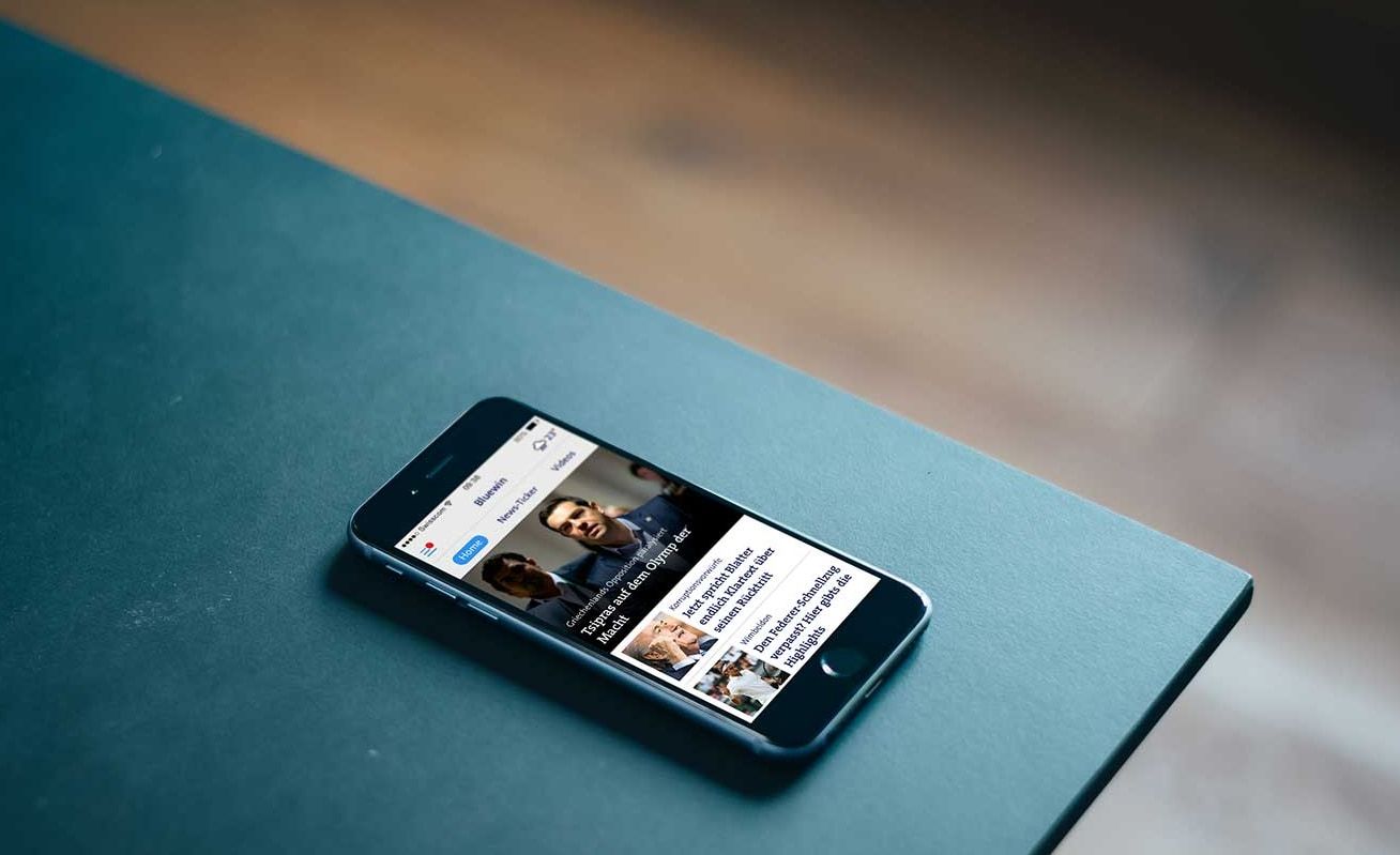 Smartphone on a teal desk showing the Bluewin news portal